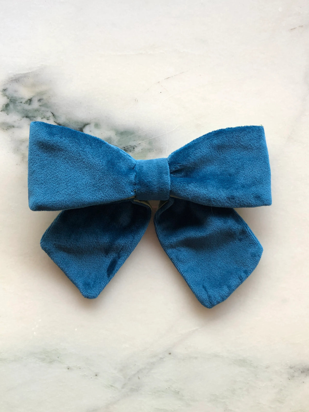 Broochella men's handmade Small Velvet Bow Brooch in rich peacock blue velvet with contrasting lime green lining, featuring a designer double bow with softly sculptural loops, photographed on white marble.