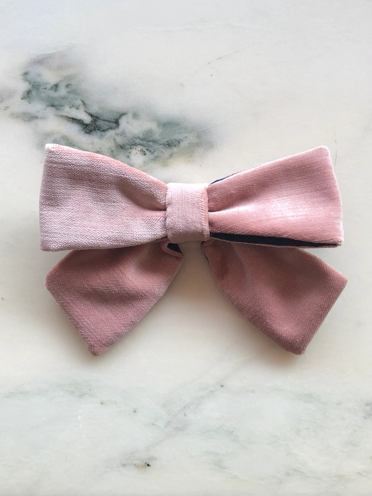 Broochella handmade Small Velvet Bow Brooch in soft blush pink velvet with contrasting navy lining, featuring a designer double bow with sculptural loops, photographed on white marble.