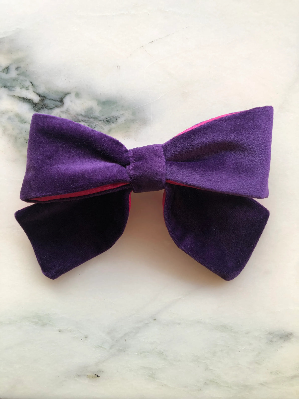 Broochella men's handmade Small Velvet Bow Brooch in deep purple velvet with contrasting vibrant fuchsia lining, featuring a designer double bow with softly structured loops, photographed on white marble.