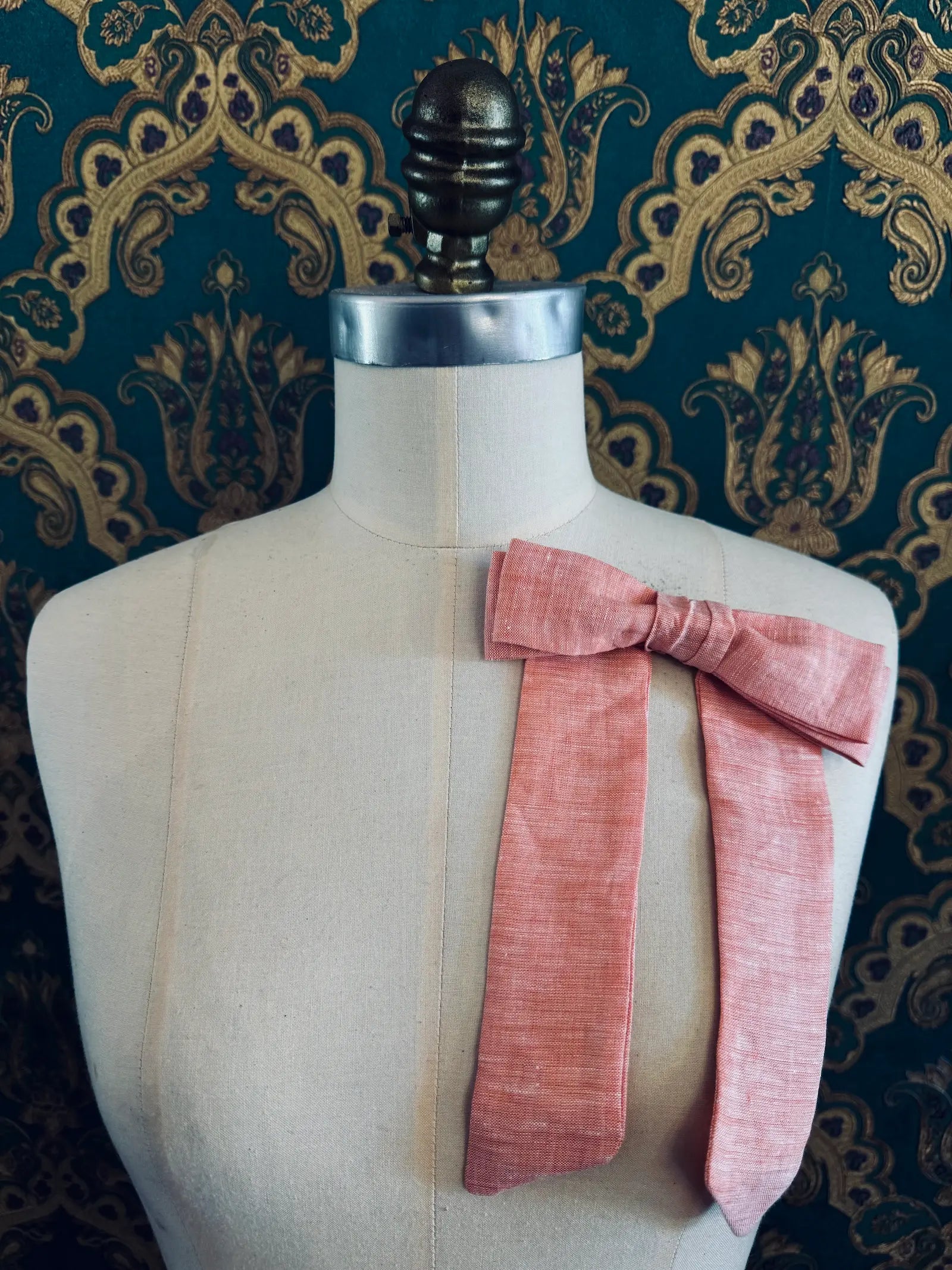 Broochella  Sofia handmade linen bow brooch in peach. Pictured on a mannequin. The background is green and gold damask wallpaper.