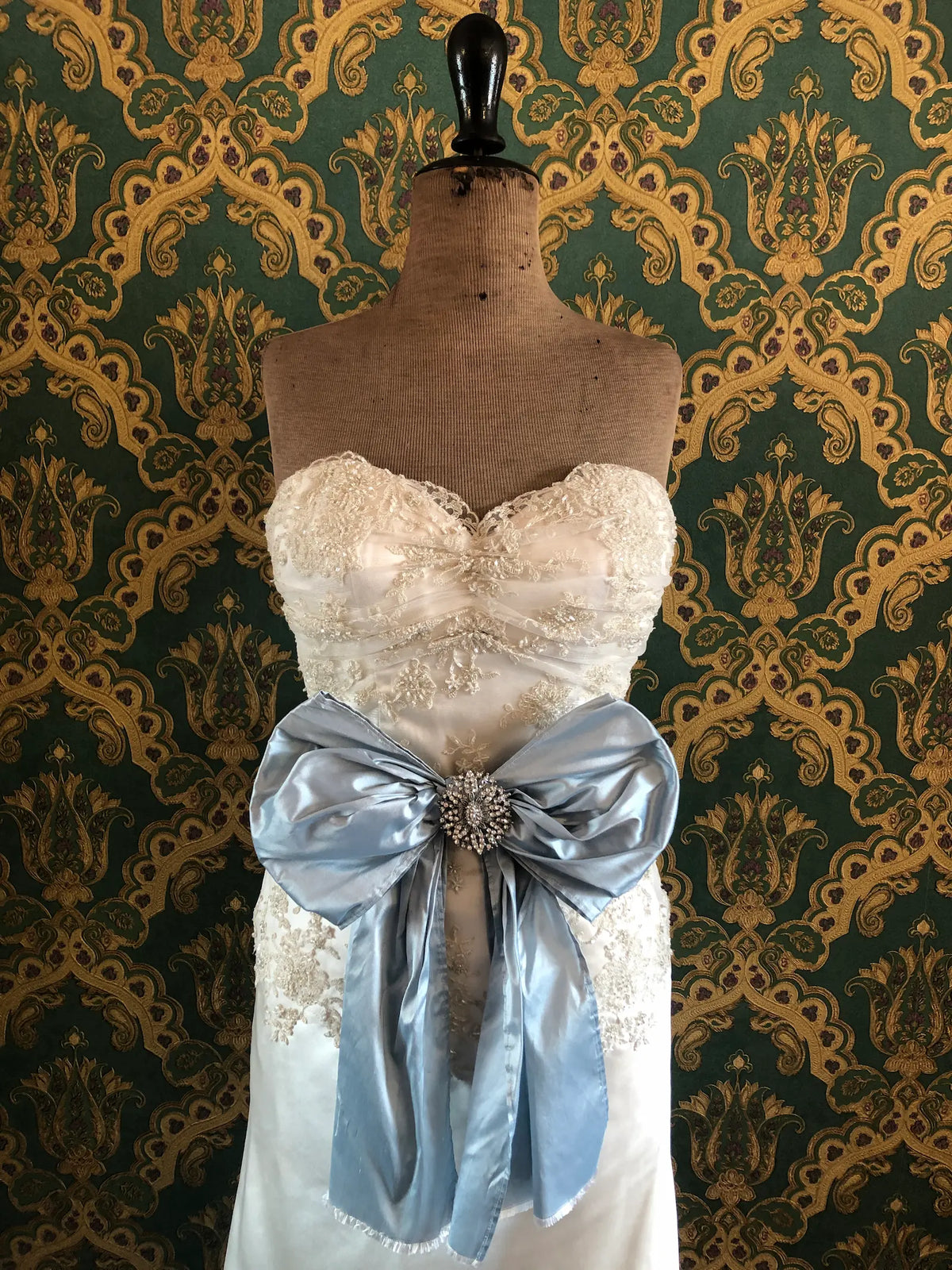 Broochella Something Blue Silk Bow in powder blue with an ornate oval crystal brooch centre and long flowing silk tails, photographed on a white marble background.