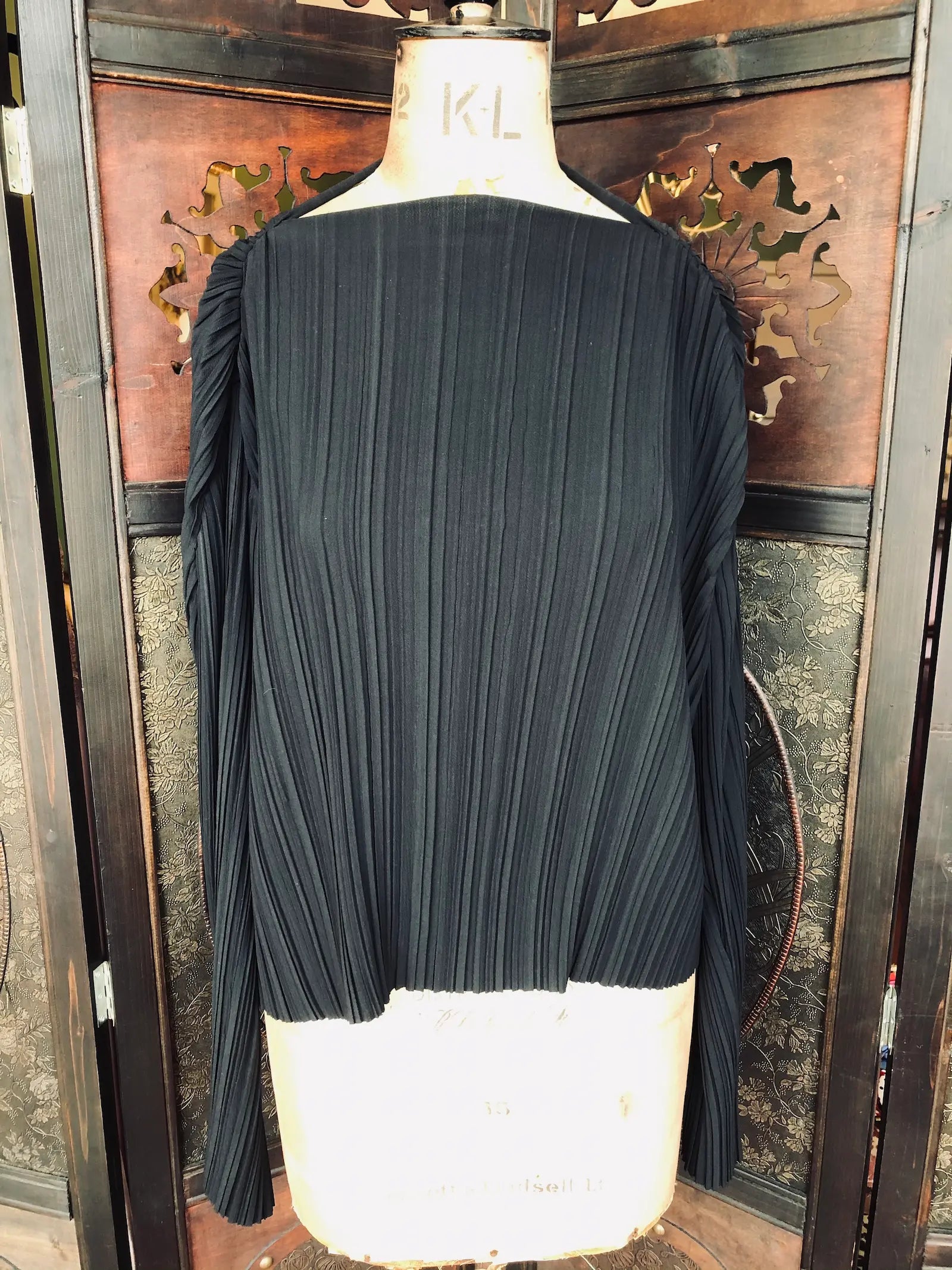 Broochella Stockholm Atelier & Other Stories black long sleeved pleated mesh  on a mannequin against a decorative wall.