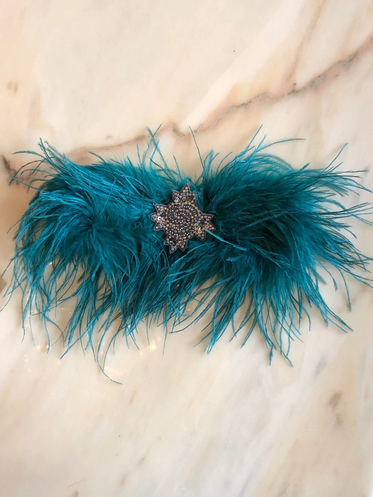 Broochella handmade Teal Feather Bow Brooch featuring dramatic ostrich feathers and an ornate jewelled centre, an oversized designer statement fashion accessory photographed on a white marble background.