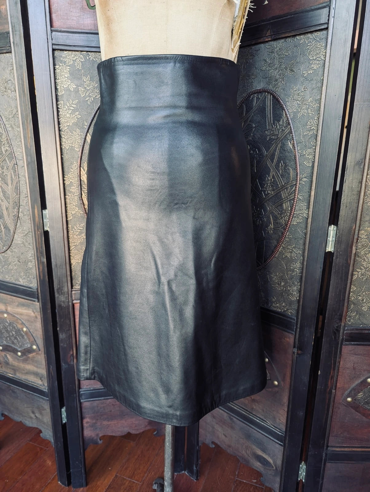 Scanlan Theodore Black Leather Skirt – AU 8 / US 4. Pictured on a mannequin. The background is an ornate dark wood screen. 