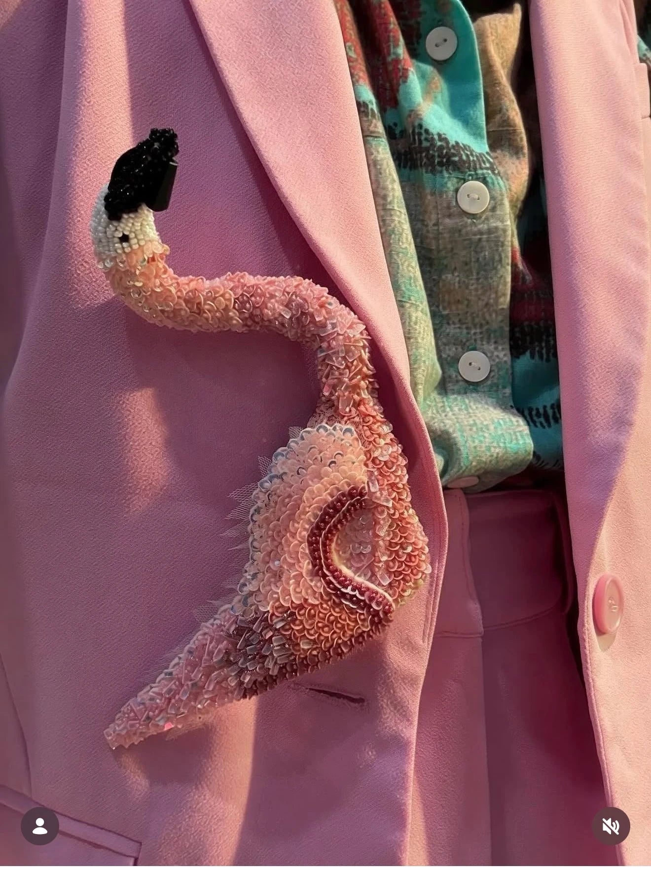 The Broochella men's hand beaded pink figural flamingo brooch. It is pinned to a men's pink suit, with a green patterned shirt. 