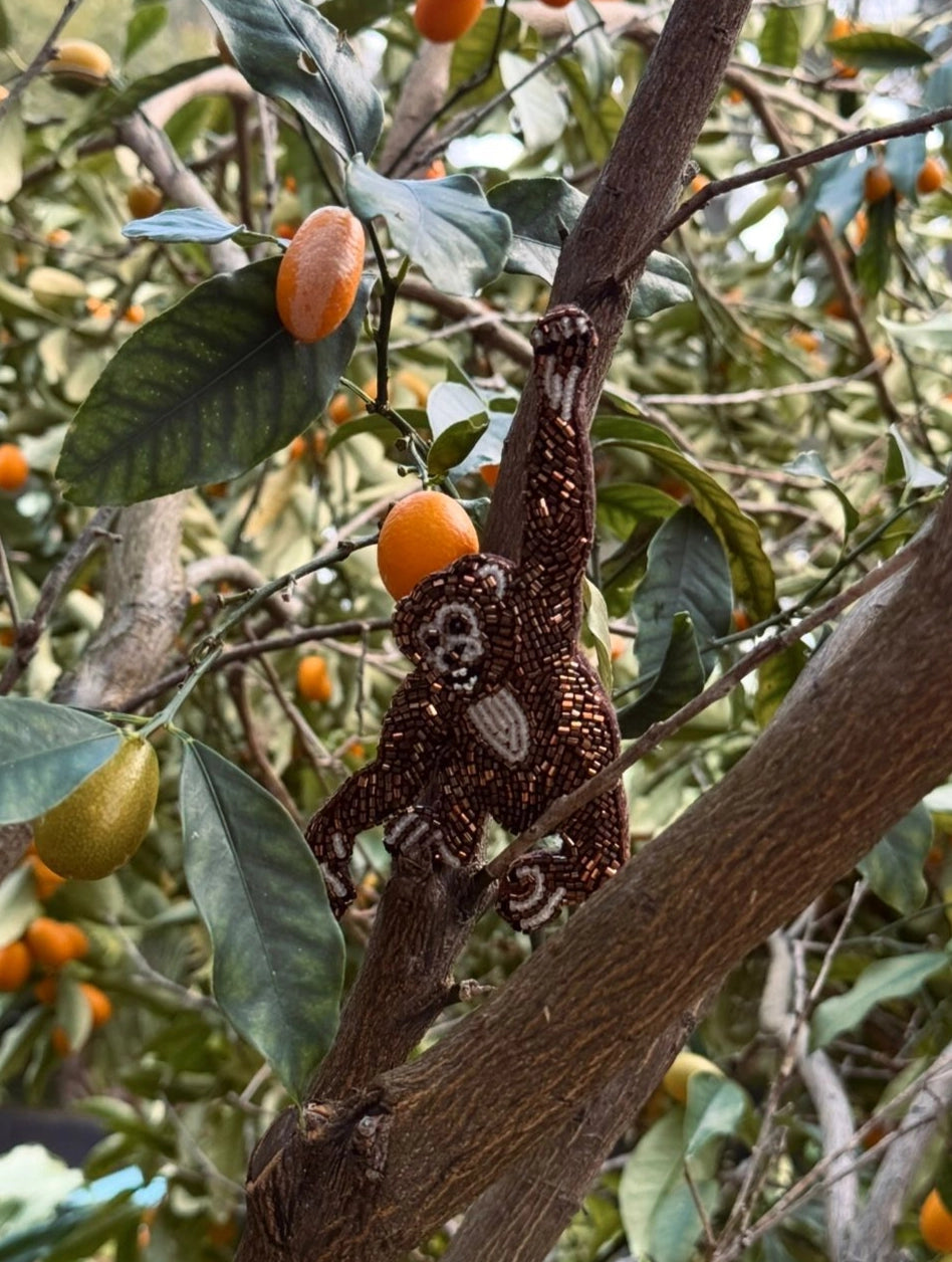 Broochella Tropicana hand beaded monkey brooch placed among orange fruits on a tree
