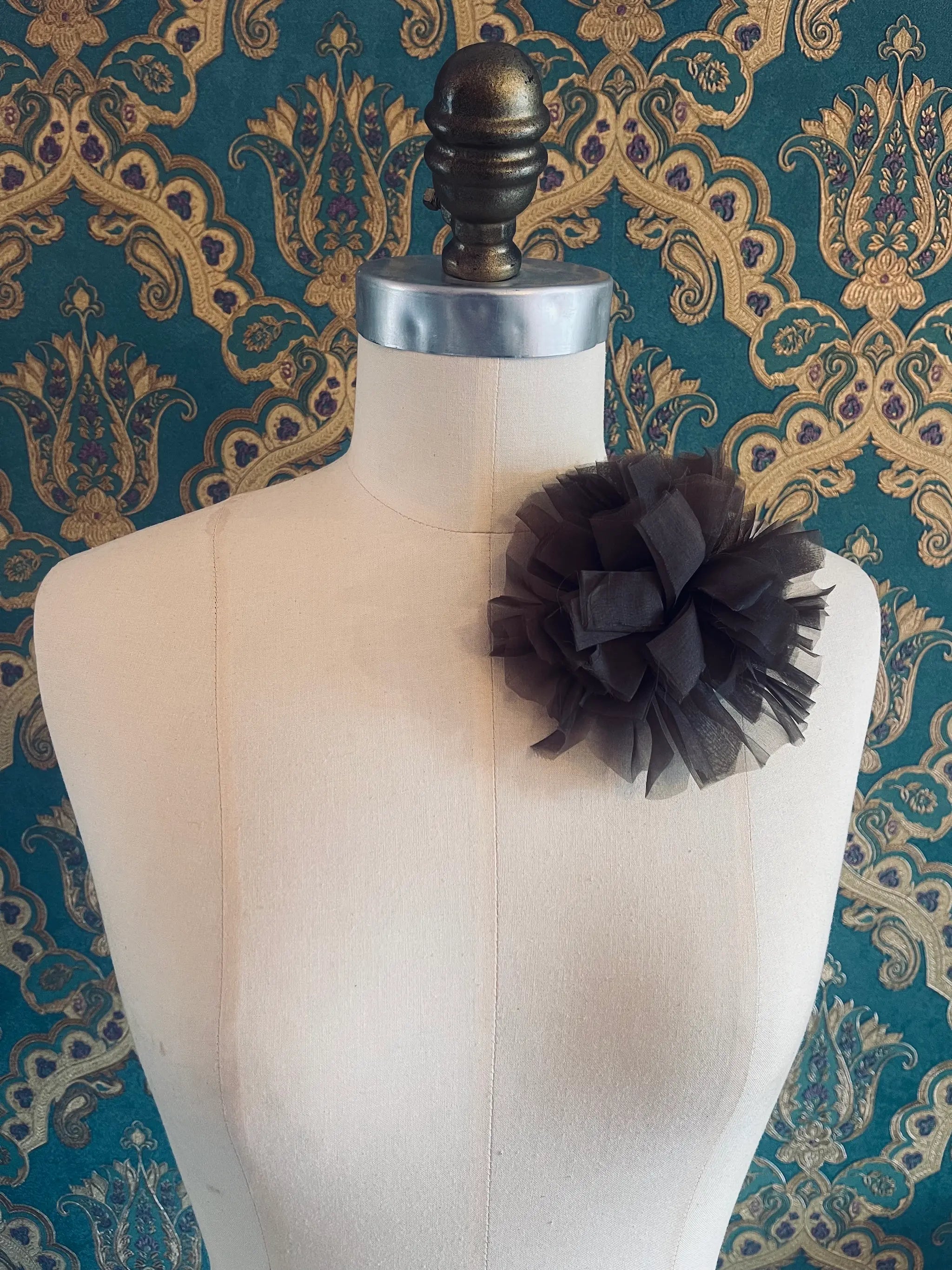 Broochella brown handmade fabric flower brooch. Pictured on a mannequin. The background is green and gold damask wallpaper