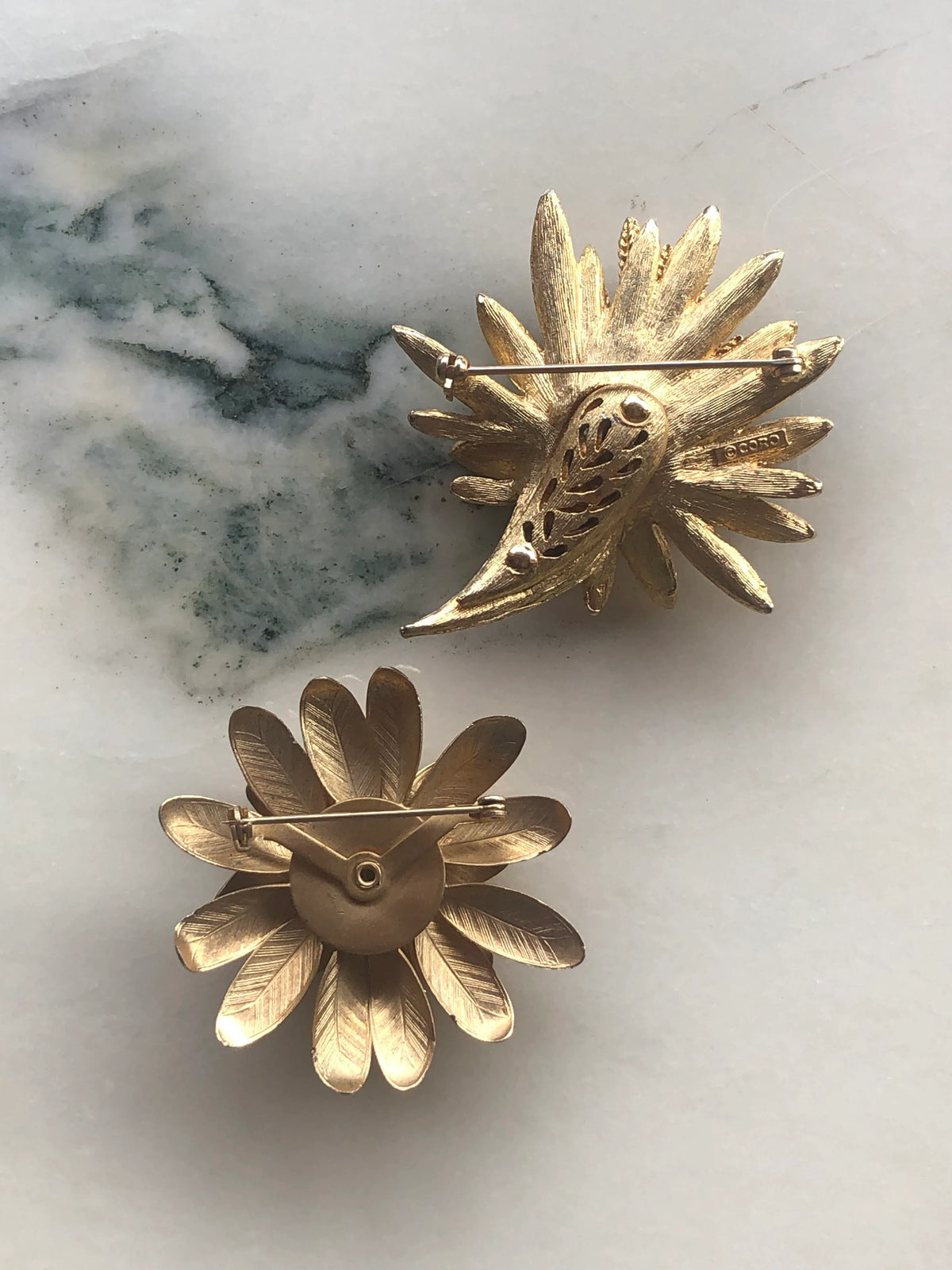 Broochella Two Golden Blooms Vintage Brooch Set back view showing the gold-tone metalwork and pin fastenings, photographed on white marble with soft grey-green veining.