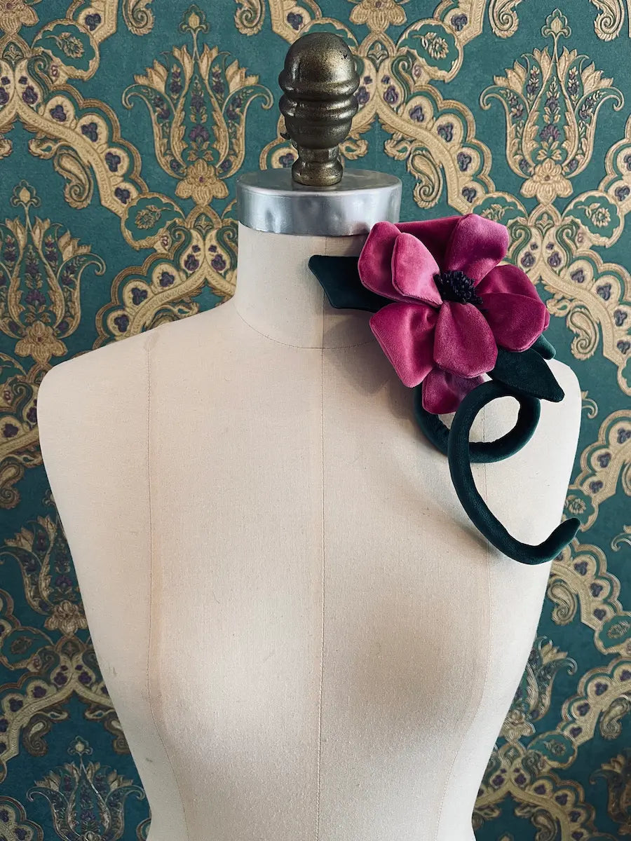Broochella Velluto Magenta handmade velvet flower designer brooch with stem and leaves. Styled on a mannequin. The background is green and gold damask wallpaper