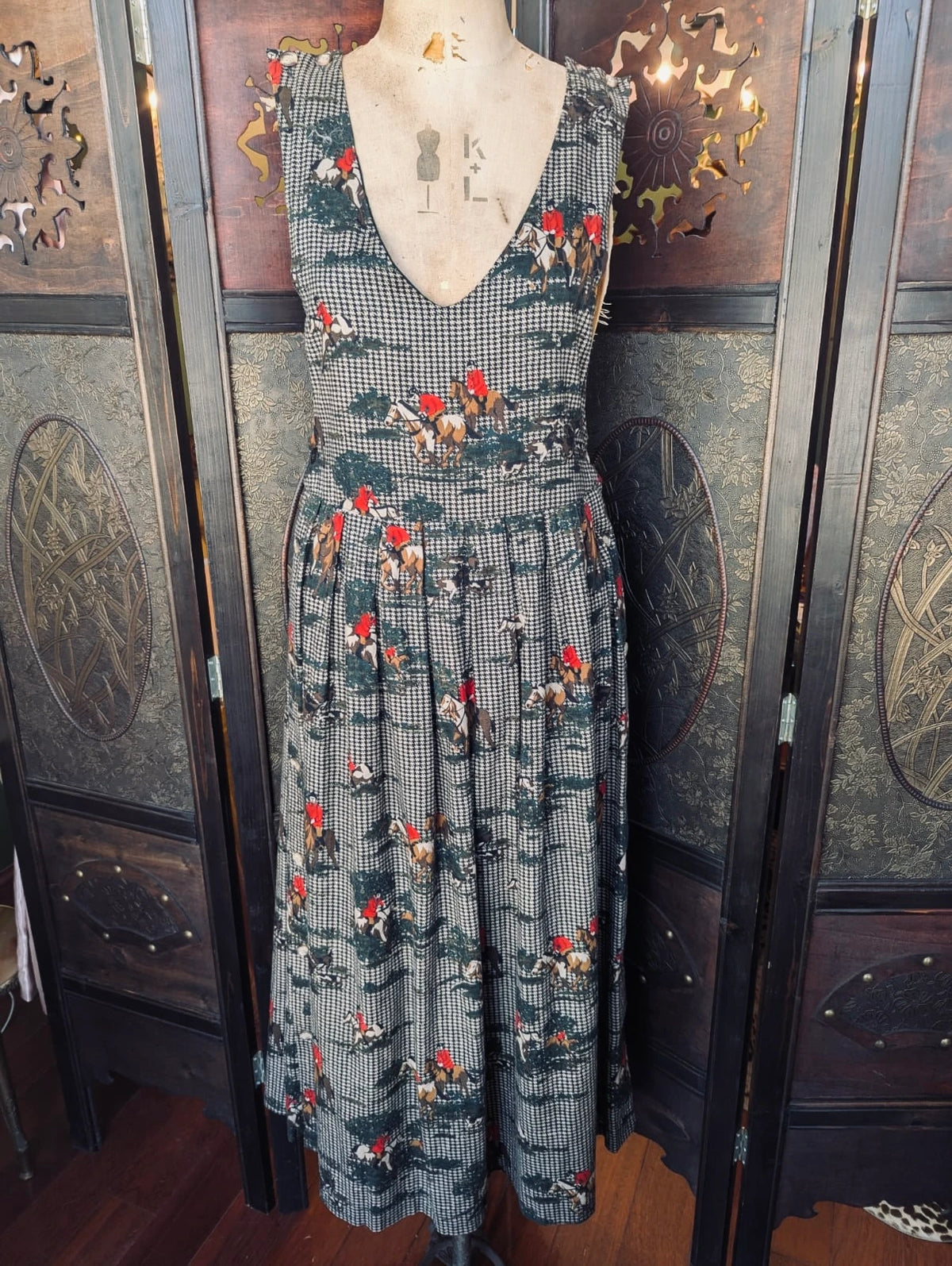 Broochella Vintage Charter Club by Jane houndstooth and equestrian print midi pinafore dress. It is presented on a vintage mannequin. The background is an ornate dark wood room divider. 