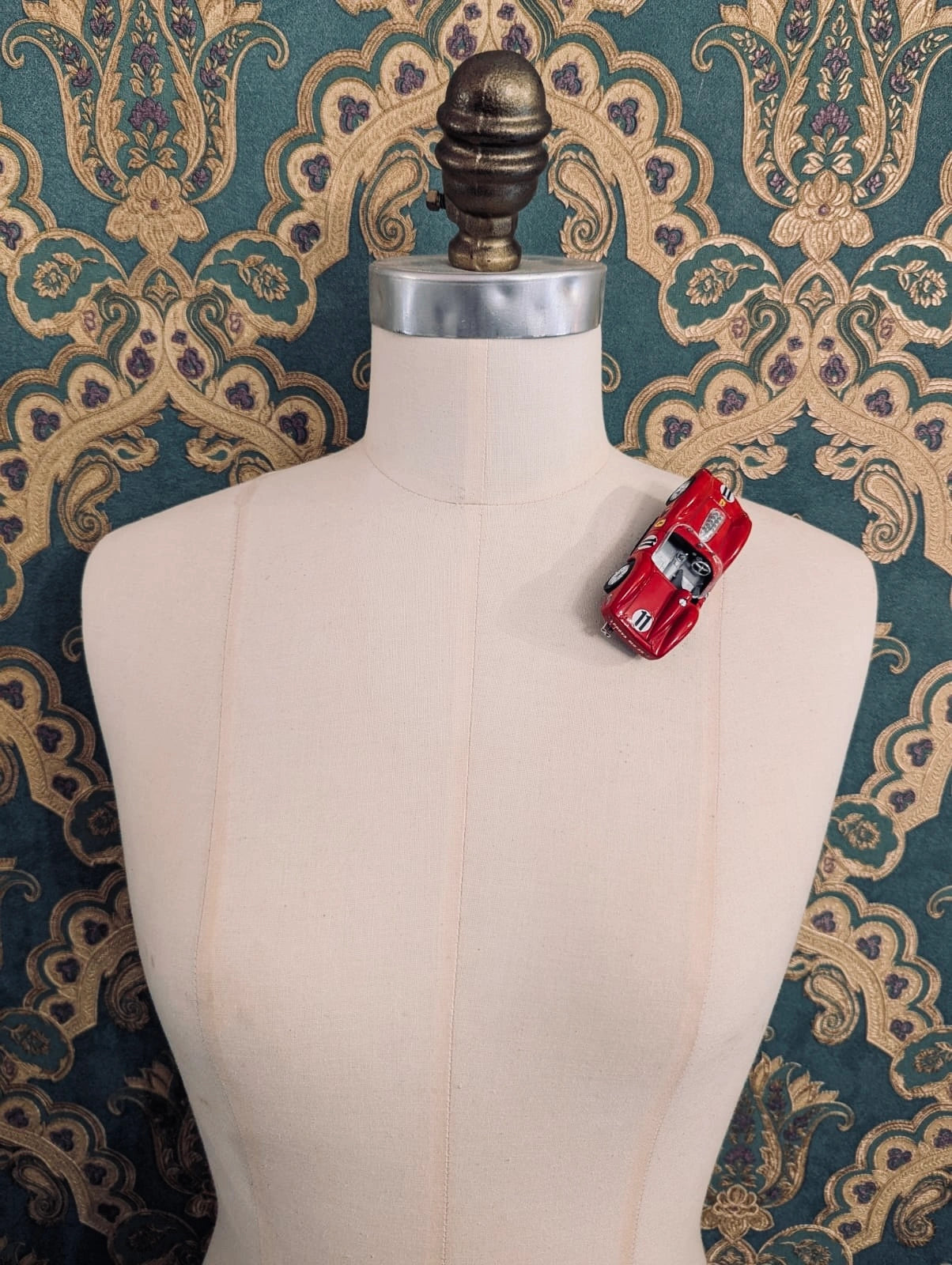 Broochella  scuderia d'oro rosso sprint number 11 red vintage formula one racing car brooch. Pinned on a mannequin. The background is green and gold damask wallpaper.