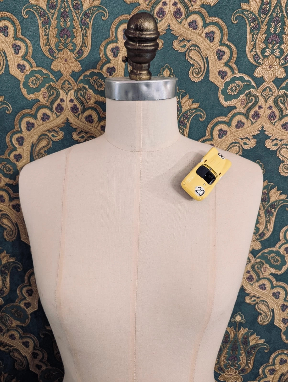 Broochella  scuderia d'oro giallo corsa 20 yellow, vintage formula one racing car brooch. Pinned on a mannequin. The background is green and gold damask wallpaper. 