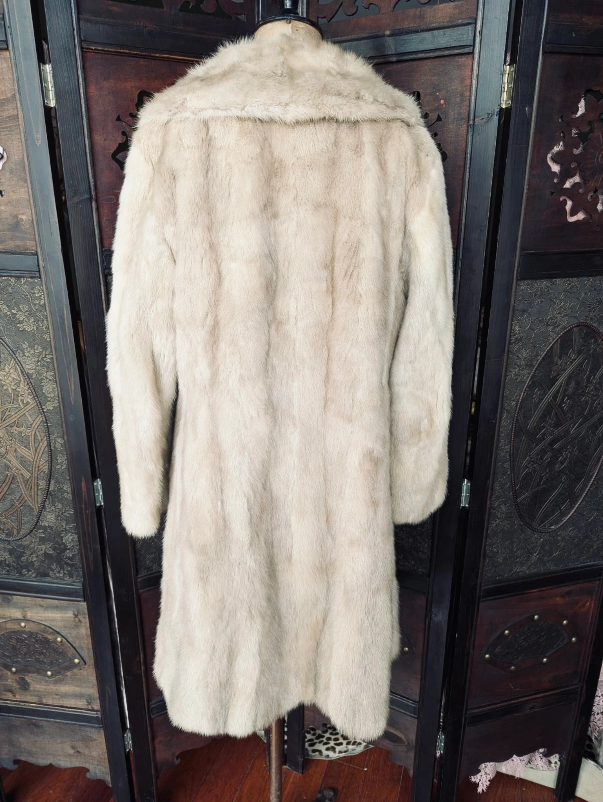 A Broochella  long vintage cream-colored fur coat displayed on a mannequin torso in front of a dark wooden folding screen.
