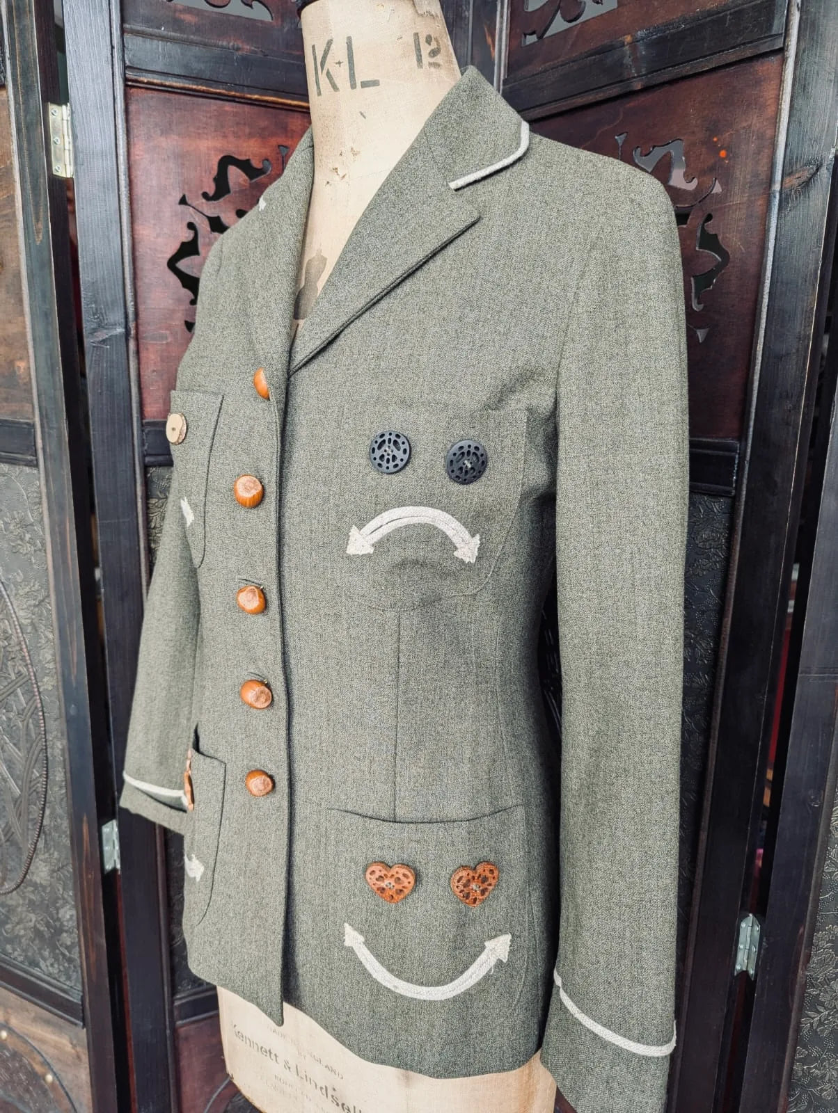 The side view of Broochella authentic designer Moschino Cheap and Chic Vintage green jacket with brown button faces on a mannequin against a dark background. 