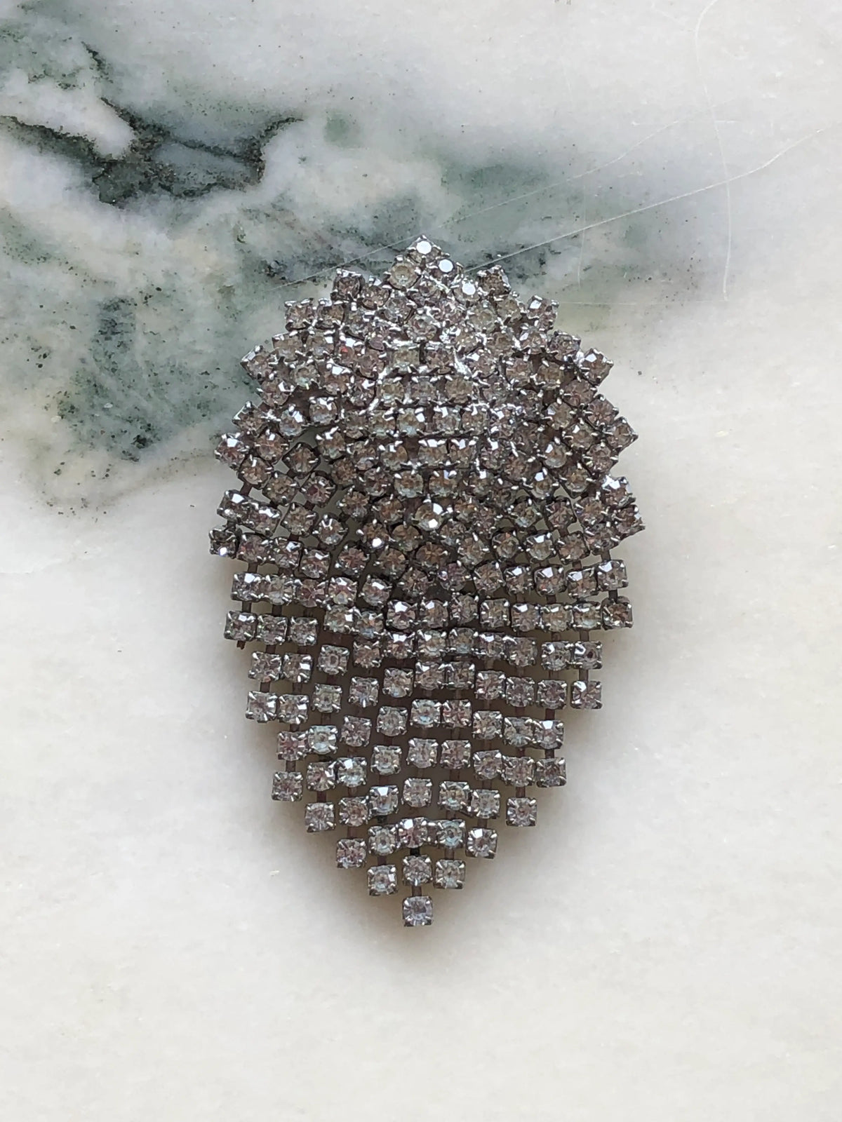 Broochella Vittoria vintage crystal cascade brooch with clear rhinestones in a silver-tone teardrop design, displayed on veined white marble.