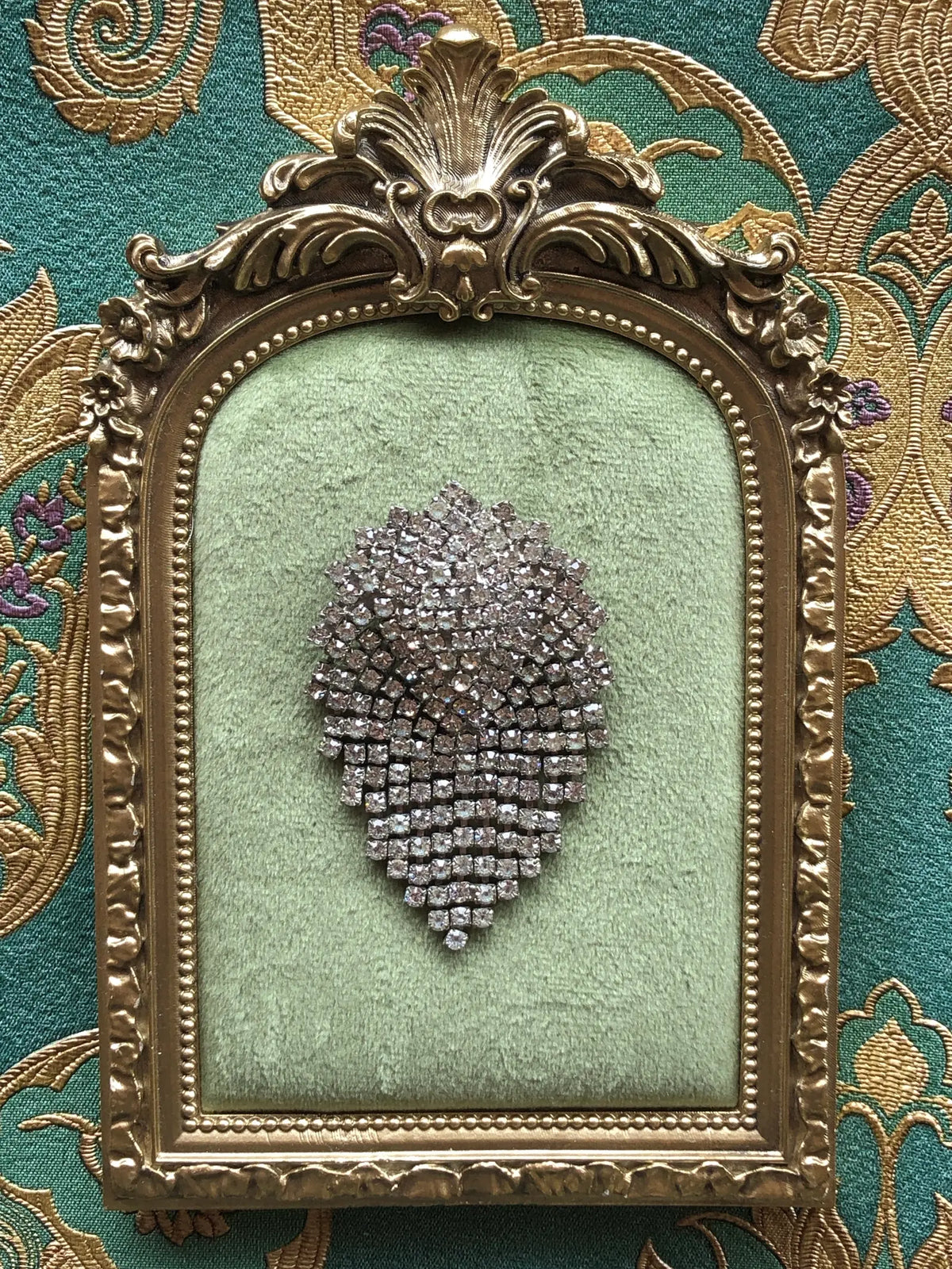 Broochella Vittoria vintage crystal cascade brooch displayed in a decorative gold frame, highlighting its sparkling teardrop silhouette.