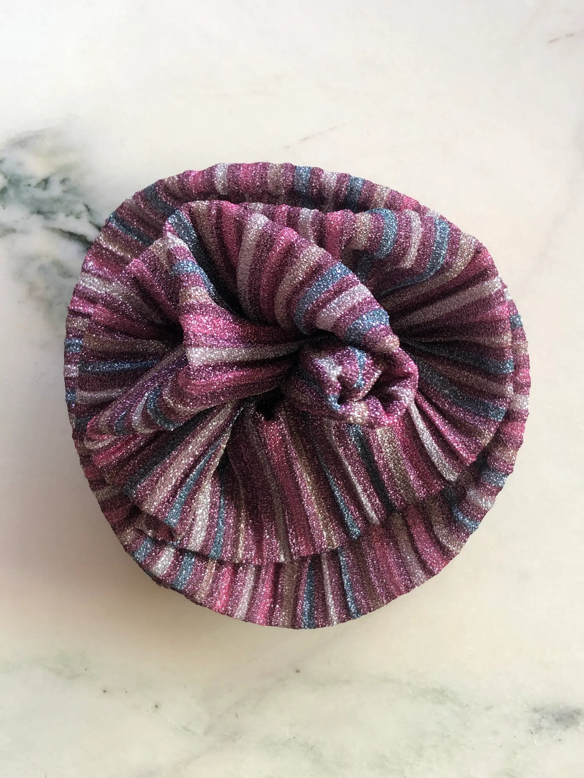 Broochella Wonka Brooch in shimmering pink pleated fabric with silver, blue and deep pink stripes, sculpted into a statement flower on a white marble background.
