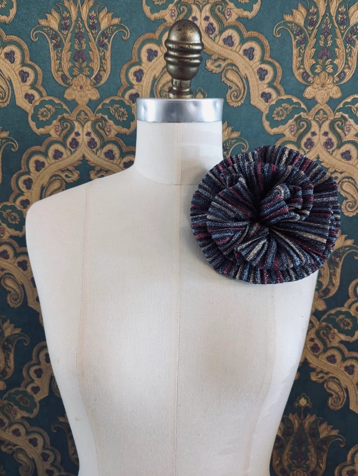 Broochella wonka handmade flower brooch in black and red striped lurex. It is pinned to a mannequin. The background is green and gold damask wallpaper.