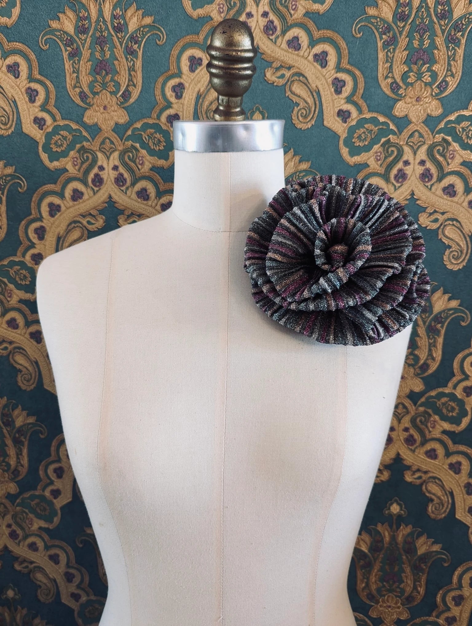 Broochella wonka handmade flower brooch in green and pink striped lurex. It is pinned to a mannequin. The background is green and gold damask wallpaper.