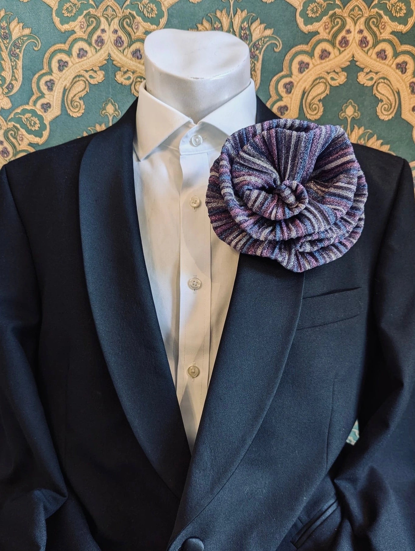 Broochella wonka handmade flower brooch in pink and purple striped lurex. It is pinned to a men's mannequin. The background is green and gold damask wallpaper.