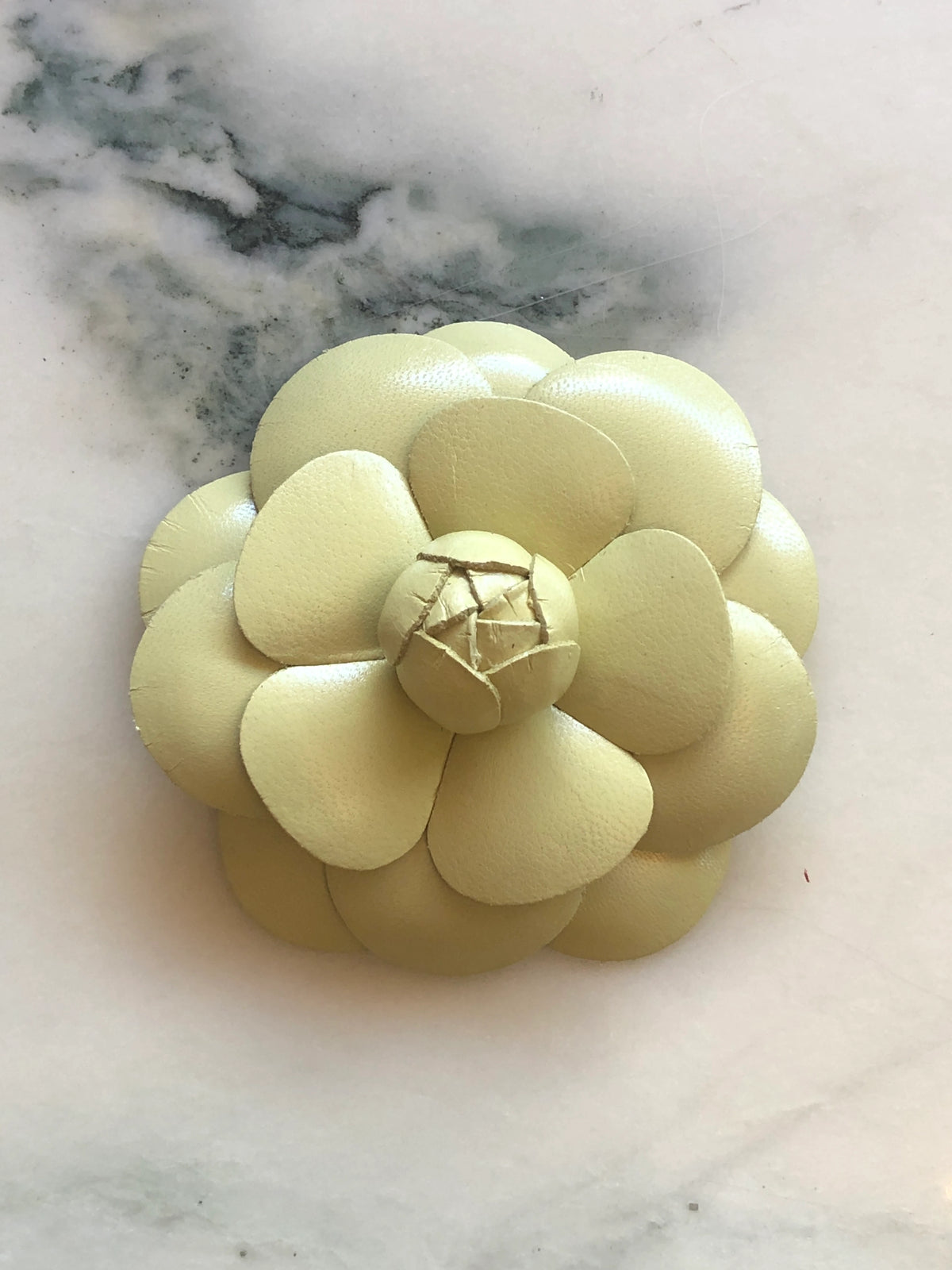 A Broochella Camelia handmade black leather flower-shaped accessory brooch,  resting on a white marble surface.