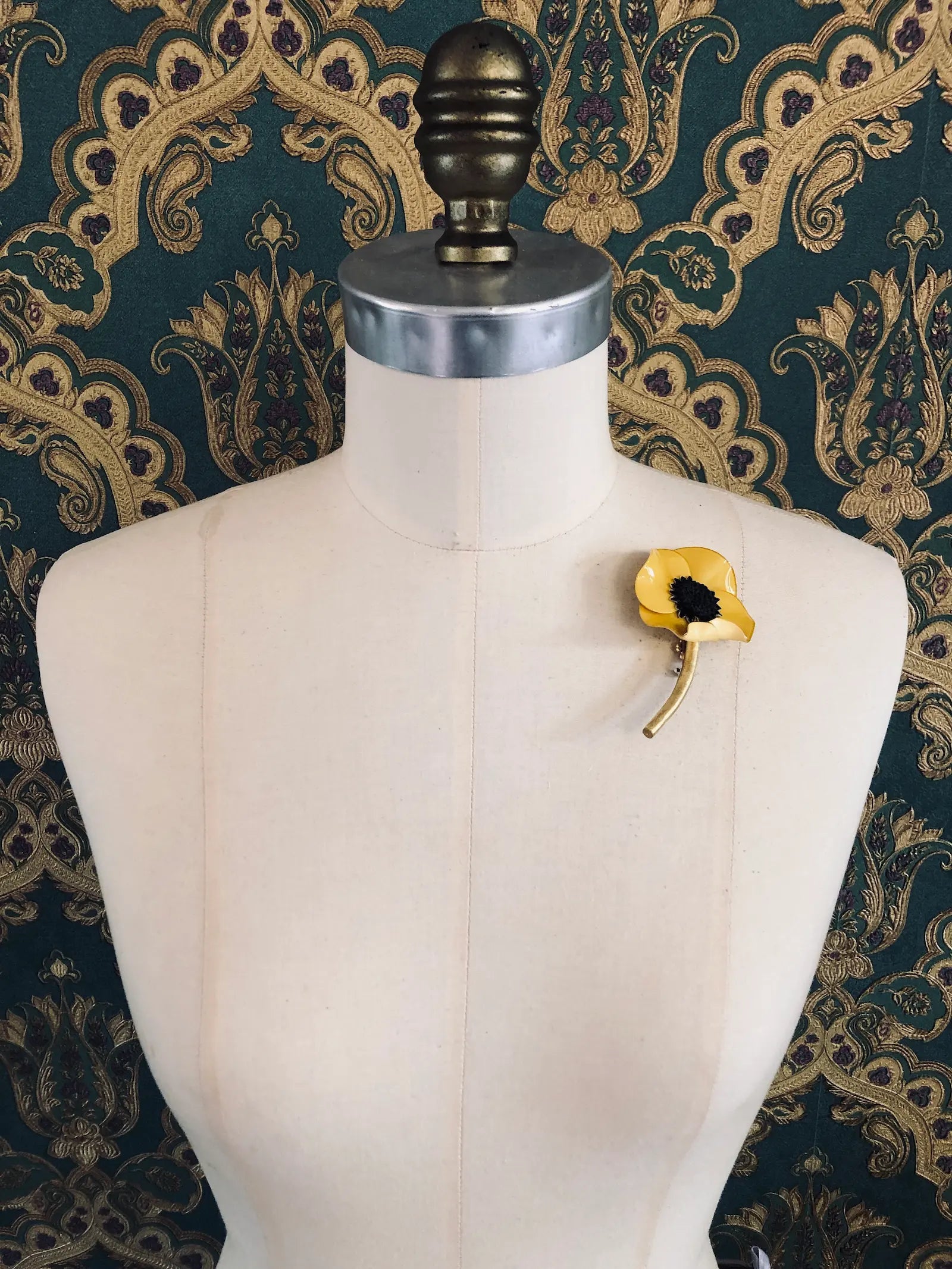 Broochella x Fabrice Paris yellow moulded acetate poppy flower brooch in red. It is pinned to a mannequin. The background is green and gold damask wallpaper. 