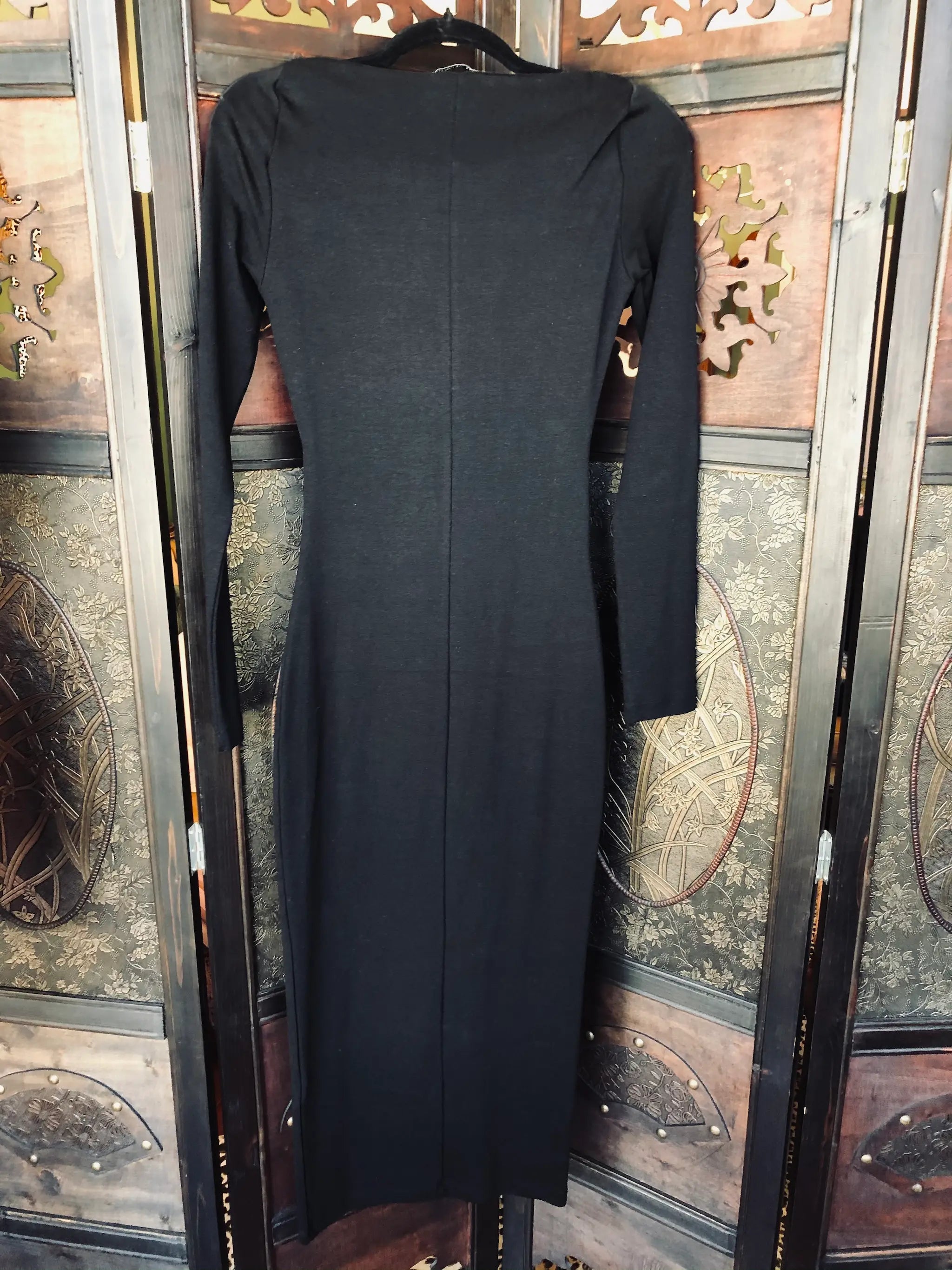 A Broochella Zara size small, black long-sleeve midi dress with a square neckline and structured shoulders, hanging on a black hanger in front of a decorative wooden folding screen.