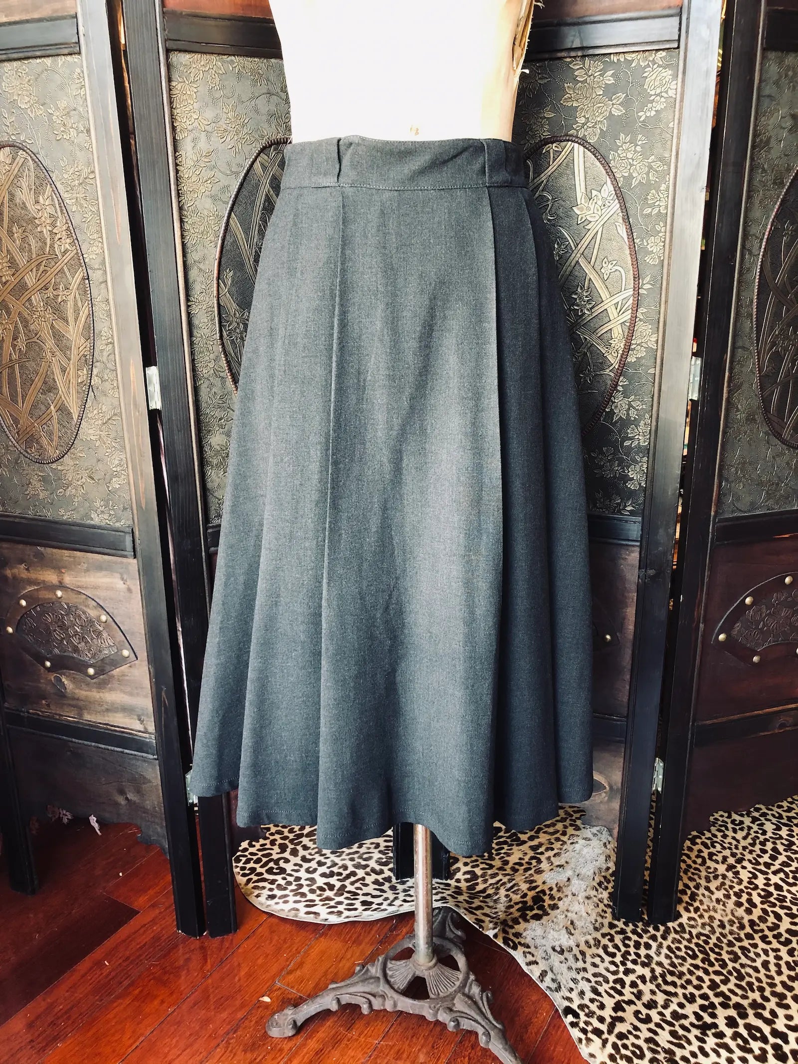 Broochella Zara grey pleated midi skirt on a mannequin in front of decorative wall panels.