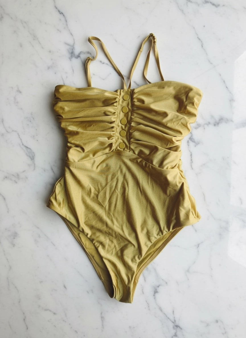 A Broochella Zimmerman mustard yellow one-piece swimsuit with a ruched corset-style bodice and thin shoulder straps, laid flat on a white marble surface.