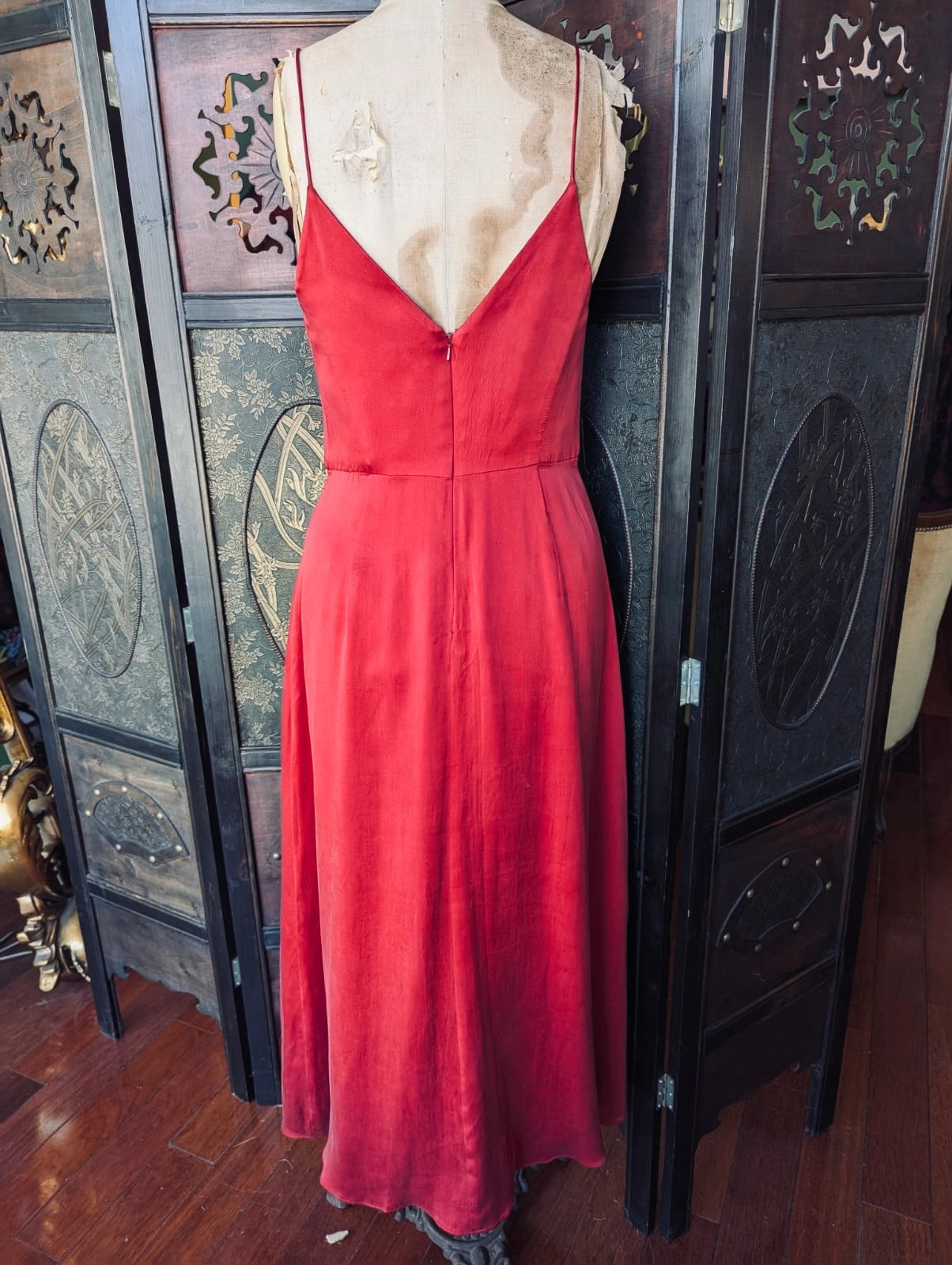 The back view of the Broochella Zimmerman designer red silk midi dress. It is pictured on a mannequin. The background is an ornate, dark wood room divider