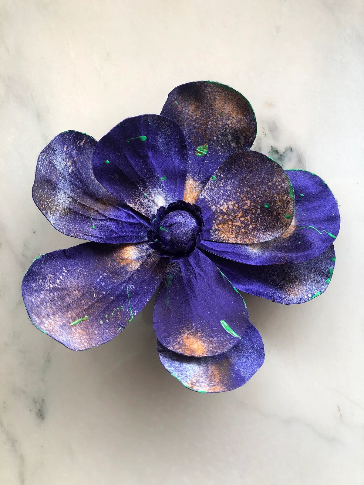 Handmade Broochella Magnolia d’Arte designer flower brooch with sculptural deep violet silk petals, individually hand-painted with bronze, white and vivid green artistic splashes, photographed on white marble.