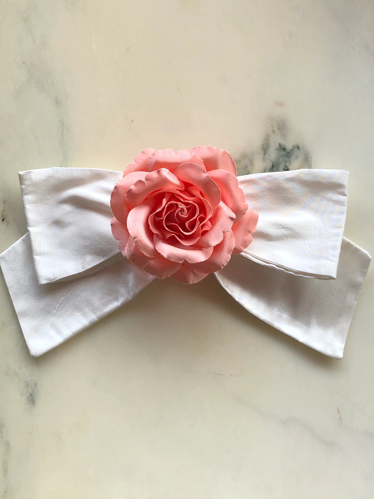 Broochella Peaches & Cream Floral Bow Brooch featuring a handmade silk ivory bow with a peach rose centre, photographed on a white marble background.