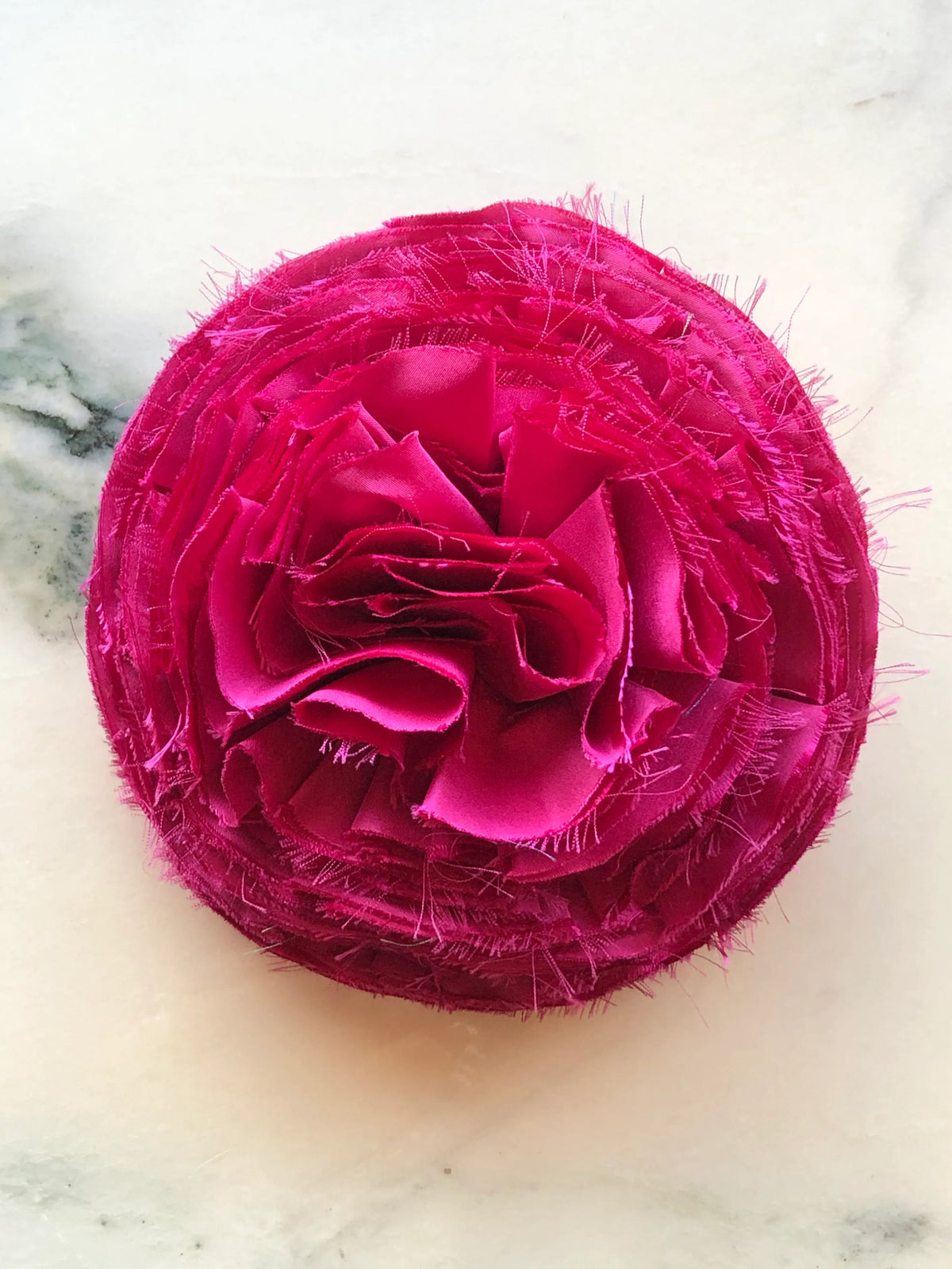 Large pink Pom Pon Flower Brooch with sculptural layered fabric petals and raw frayed edges, photographed on a white marble background with soft grey veining.