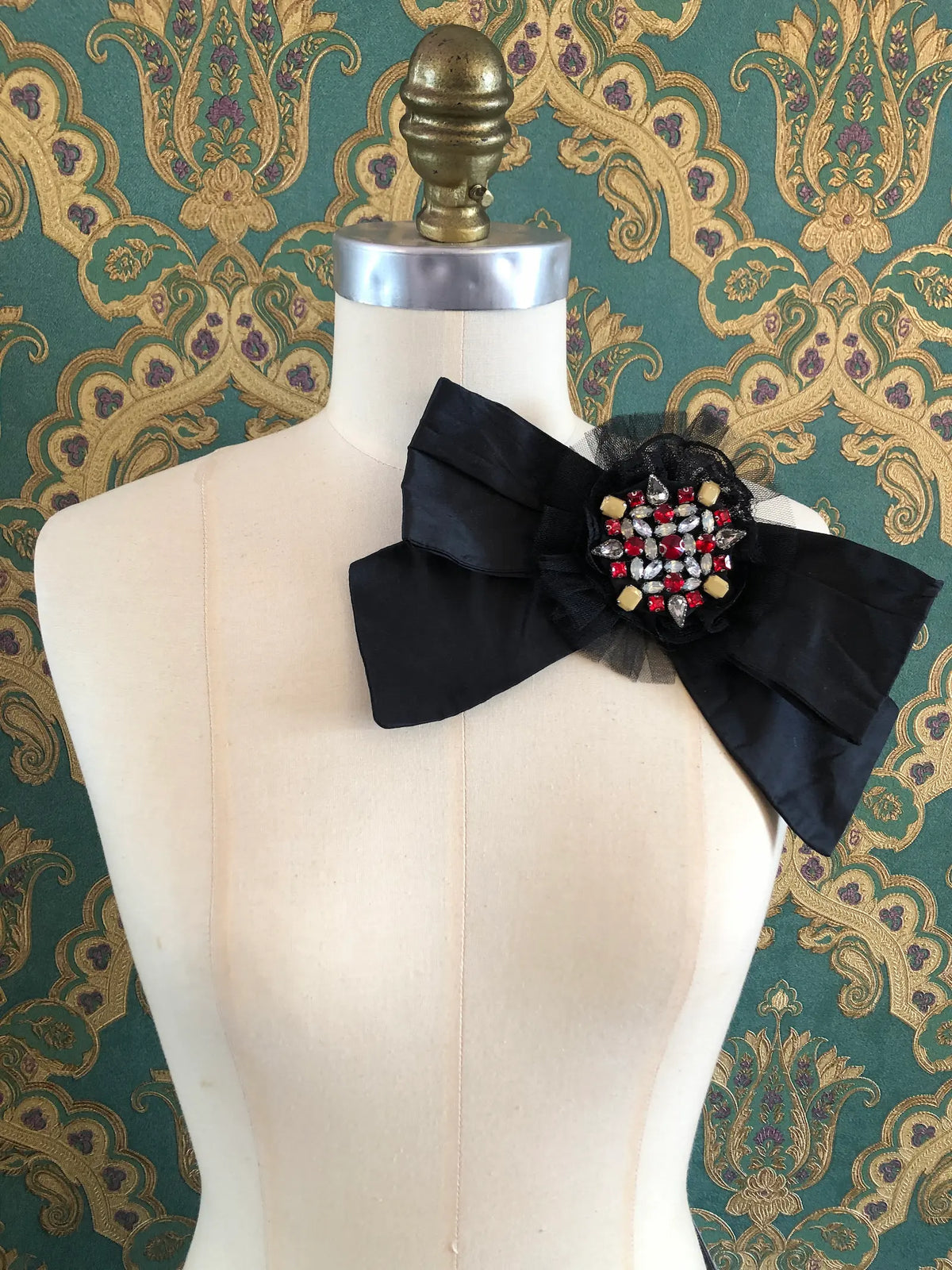 Broochella Viva Loren Bejewelled Bow Brooch in black silk with a statement crystal centre in red, clear and gold, styled on a mannequin.